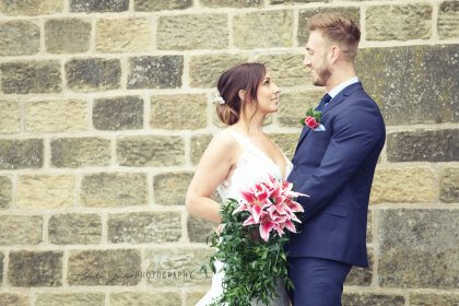 Bride and groom smiling in front of exterior wall