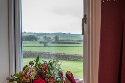 Red shoes and flower bouquet on window ledge with fields in background