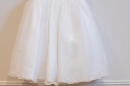 flower girl dress on hanger with bouquets of flowers on wooden floor underneath